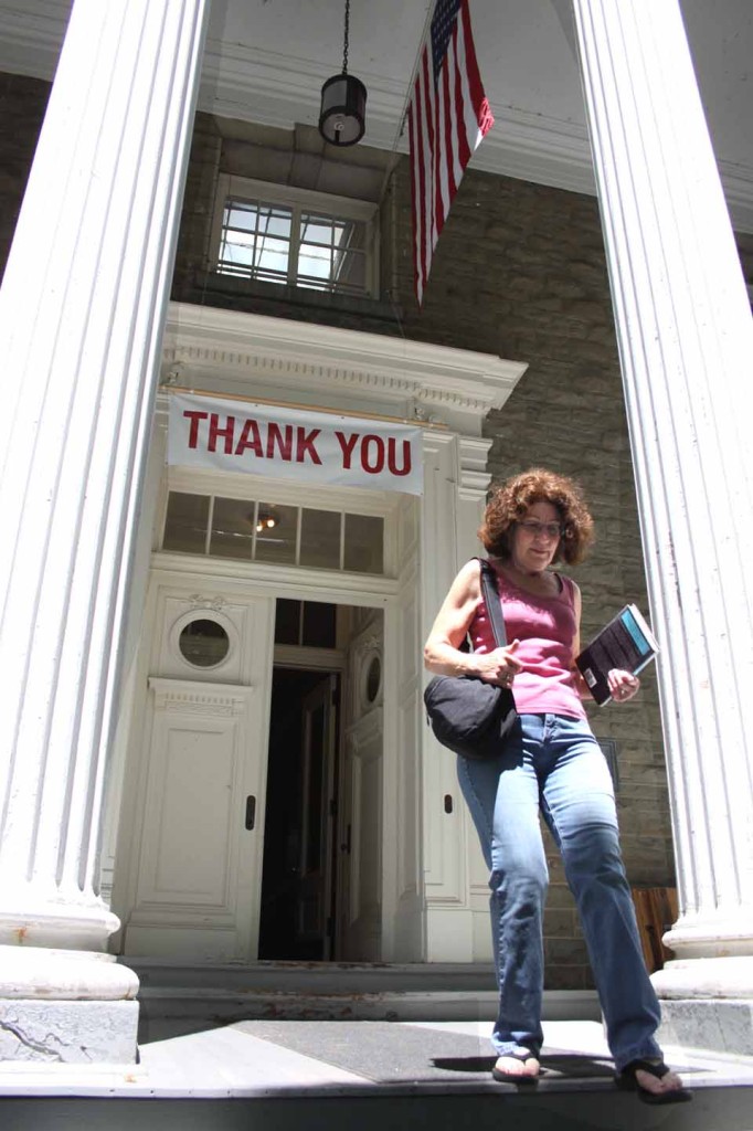 Eileen Schatzel, Burlington Flats, passes under the banner that has graced the front entrance of the Village Library of Cooperstown.  it was placed there by the village Library Board and the Friends of the Village Library after voters approved June 8 approved a dedicated source of funding for the library by an 80-20 margin.  (Jim Kevlin/allotsego.com)