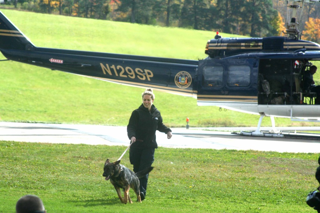 Trooper Meredith Govoni, detached from Troop K. Columbia County, to the State Police Canine Unit's training program outside Cooperstown, exits a helicopter with Lexi this morning.  The school is acclimating its dogs to flying, as the K9s can be deployed all over the state.  (JIm Kevlin/allotsego.com)